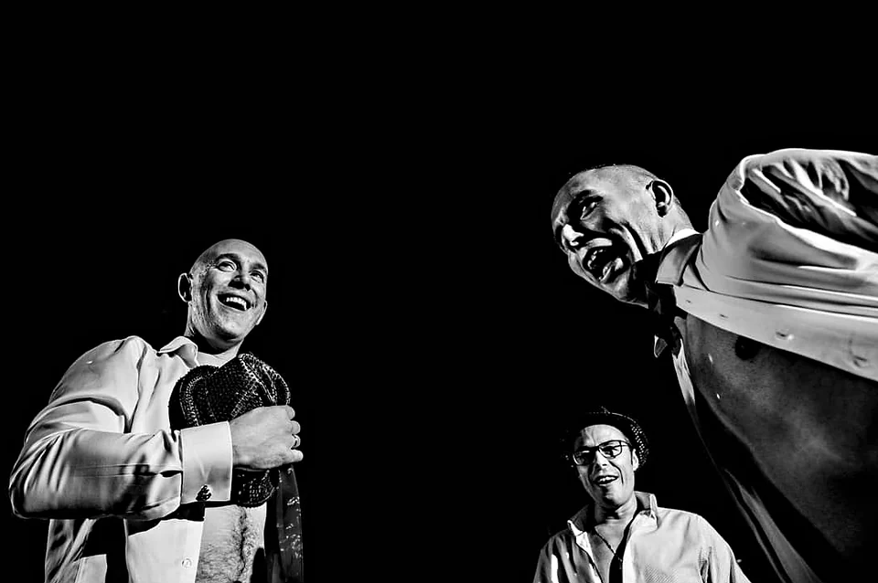 Tres invitados riendo, iluminados por un flash duro sobre un fondo completamente negro.